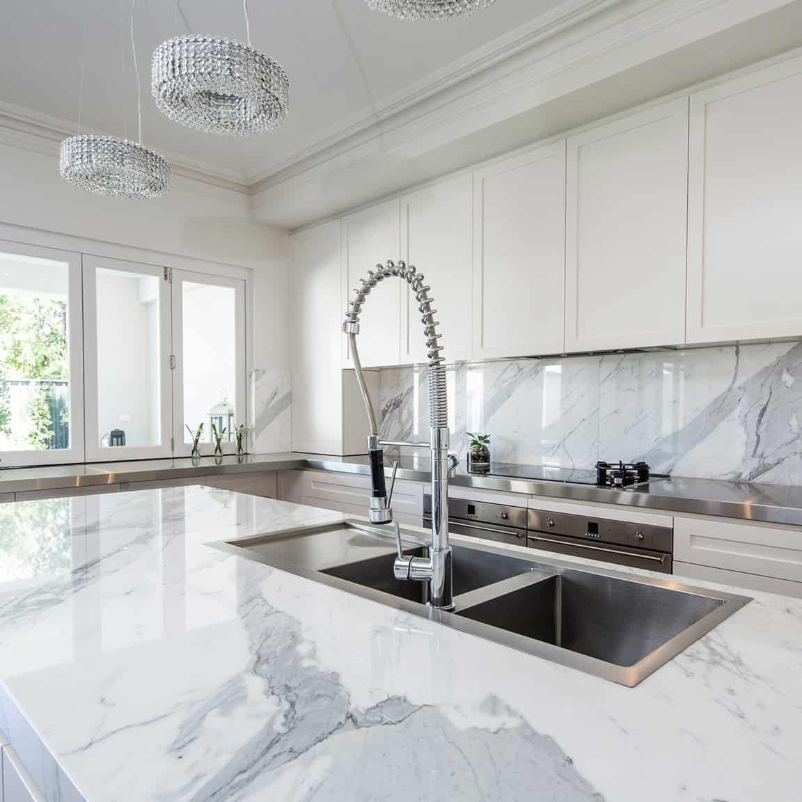 Alt="large white marble kitchen with tall mixer, marble splash back and ktichen cabinets